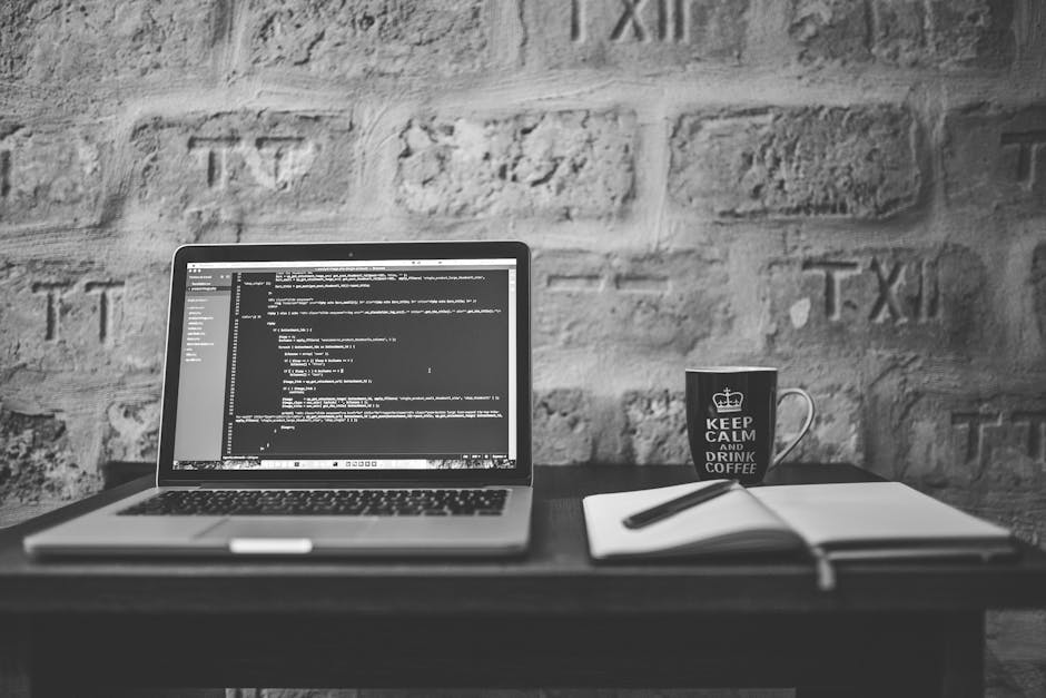 A close-up image of a laptop computer displaying lines of programming code on a dark background, with colorful syntax highlighting. Positioned to the left of the laptop is a ceramic coffee mug with a 